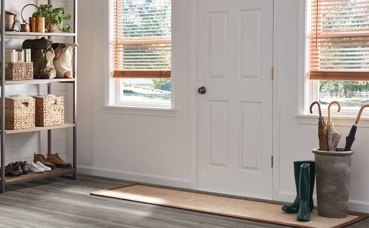 light wood blinds window treatments in entry way with white door and dark wood look vinyl flooring